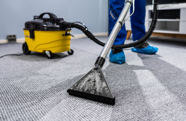 Commercial cleaner in Washington DC, Virginia, and Maryland wearing blue covers for their boots and using a steam cleaner to vacuum the grey carpet